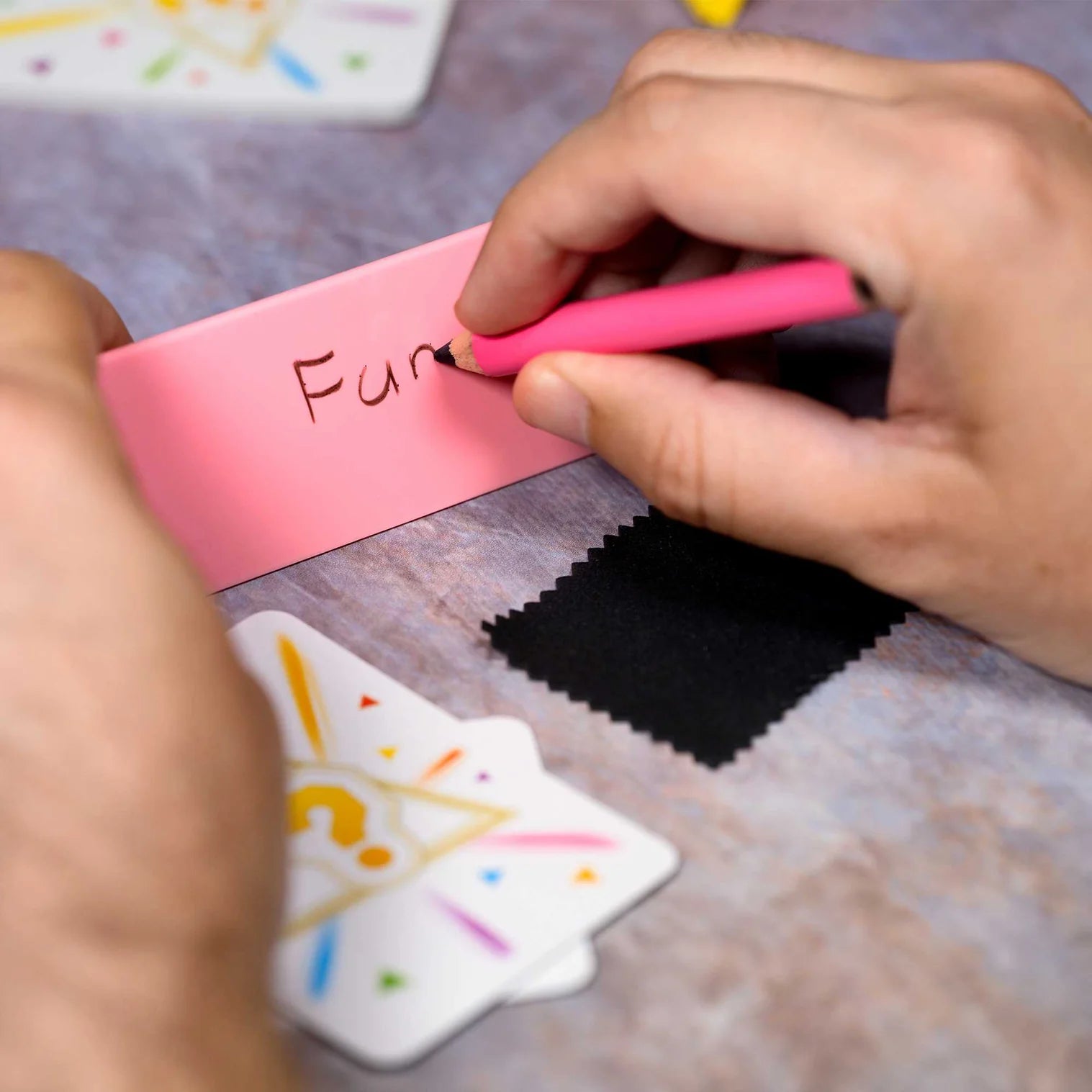 Person writing 'Fun' on a pink object with colorful background