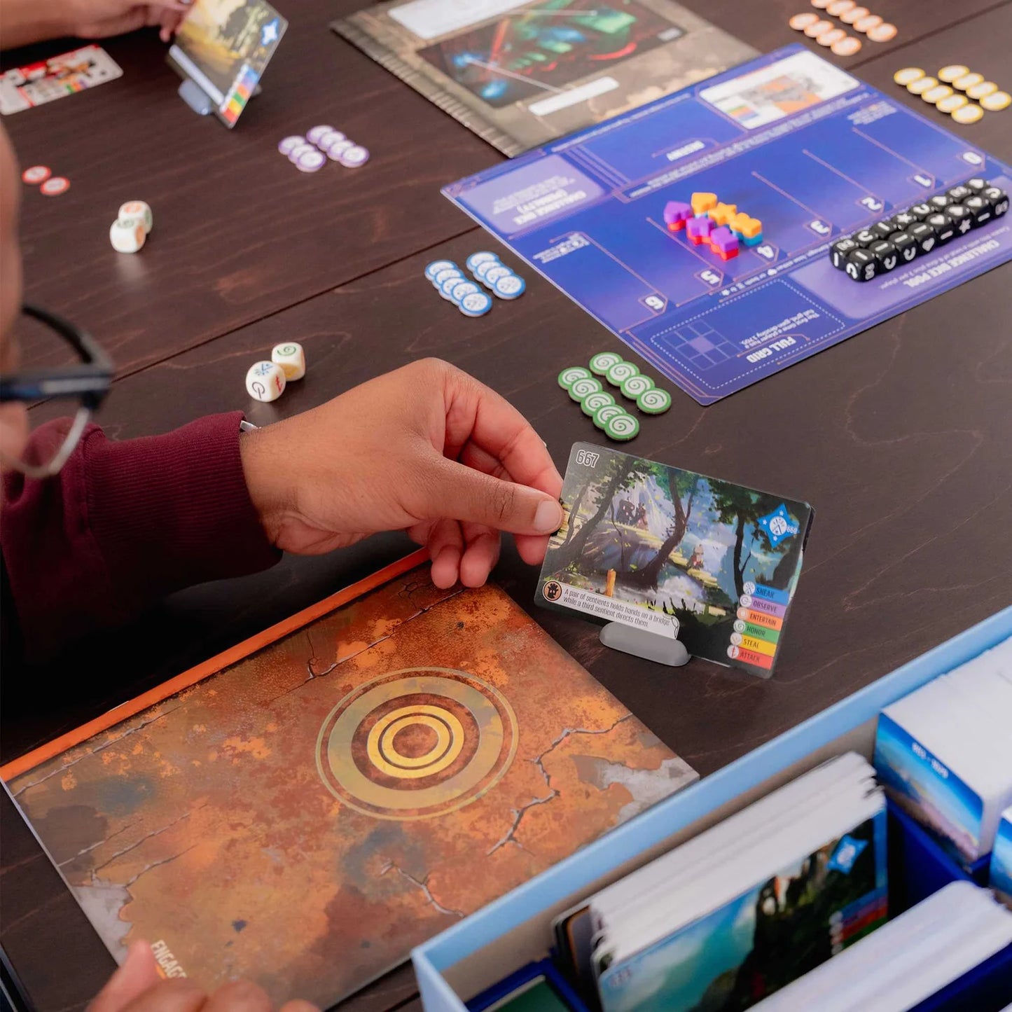 Person playing a board game with various game pieces and cards on a table.