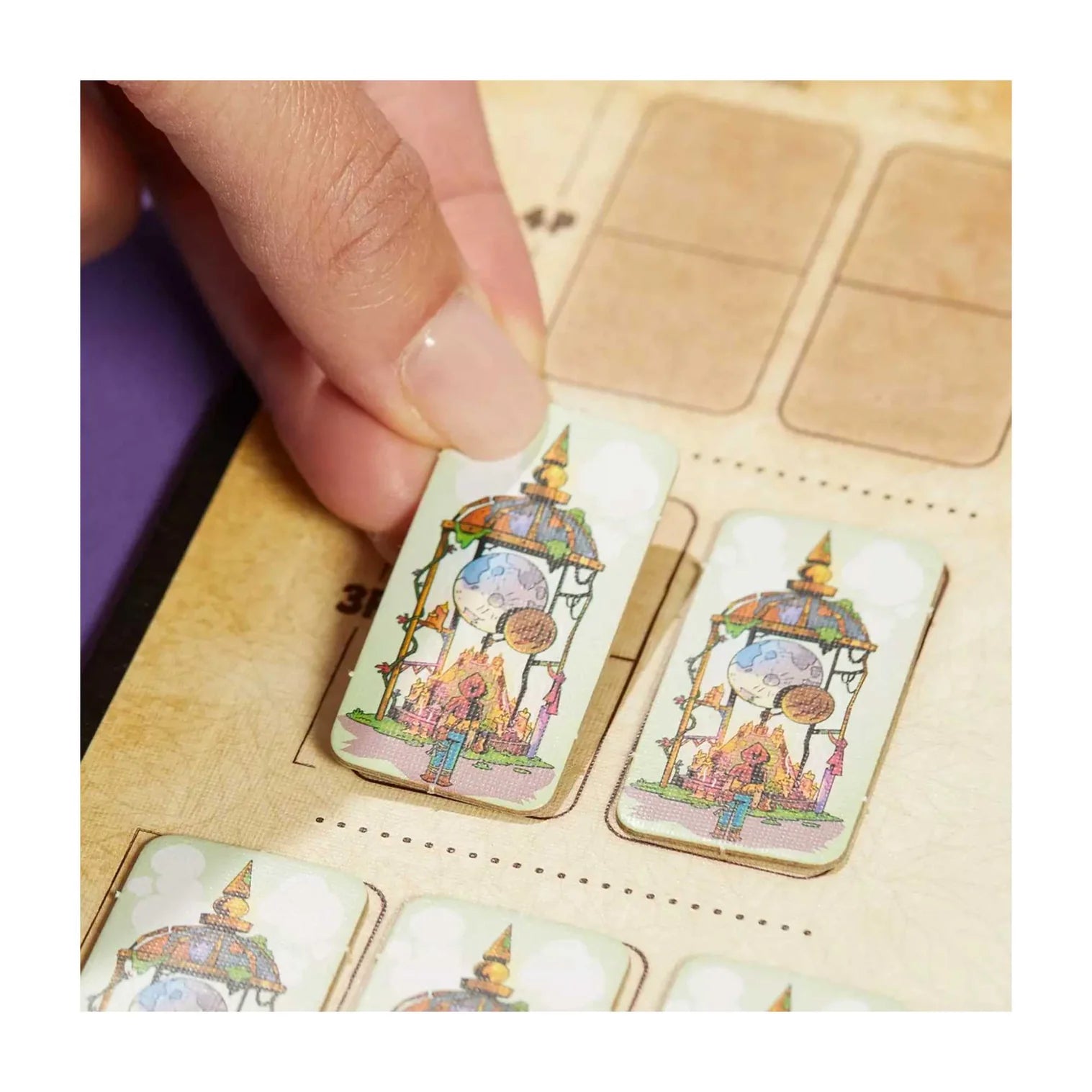 Hand holding a small card with a colorful design of a lantern and flowers, placed on a larger wooden board.