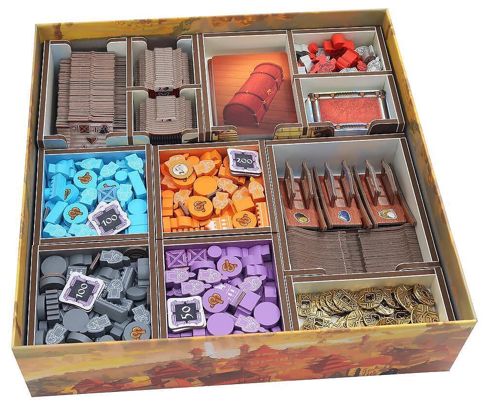 Board game box with compartments filled with various game pieces on a white background